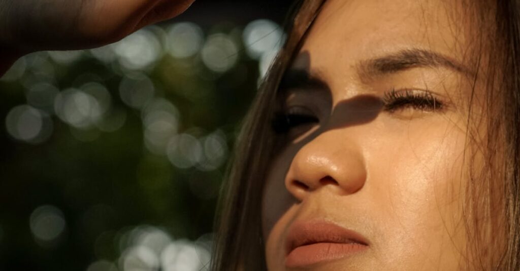 Close-up of a woman shielding her eyes while looking into sunlight, outdoors.